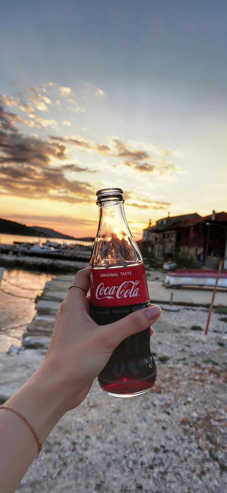 手持可口可乐玻璃瓶夕阳海景惬意生活摄影手机壁纸