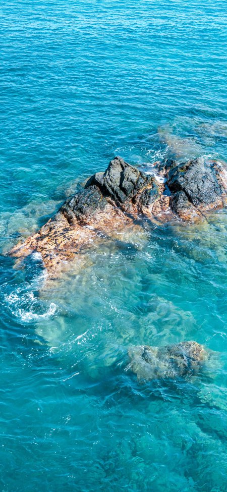 蔚蓝海水环绕褐色礁石浪花轻拍自然纹理风景手机壁纸