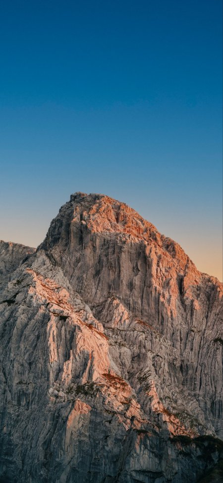 夕阳余晖映照巍峨山峰岩石蓝天风景手机壁纸