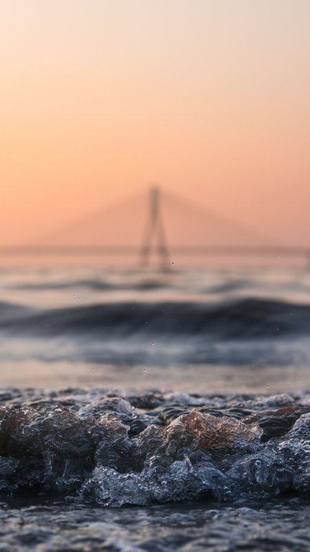 海浪拍岸远桥剪影暖橙风景手机壁纸