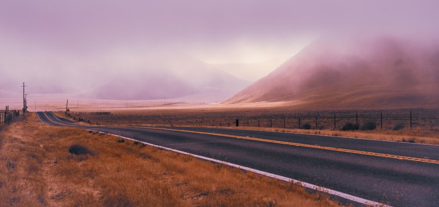 空旷公路蜿蜒穿行雾山丘间紫橙色调风景电脑壁纸