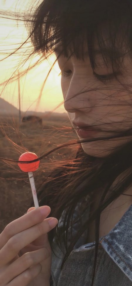 长发少女手持红色棒棒糖夕阳暖金人物摄影手机壁纸