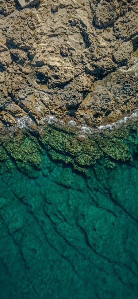 海岸岩礁与碧蓝海水交界航拍视角青绿自然风景手机壁纸