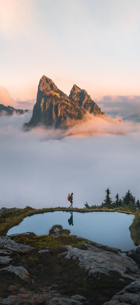 云海之巅双峰耸立背包客静立湖畔倒影粉紫自然风景手机壁纸