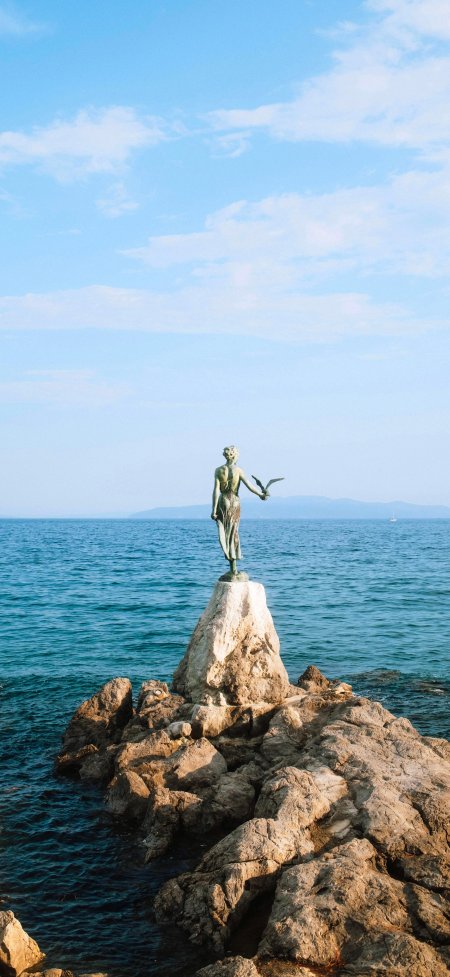 海边岩石上少女雕像手托海鸥蓝白风景手机壁纸